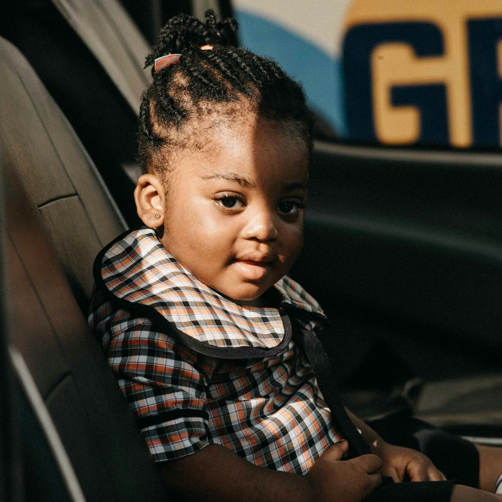 Adorable young girl seated in a car, bathed in natural sunlight, showcasing innocence and warmth.